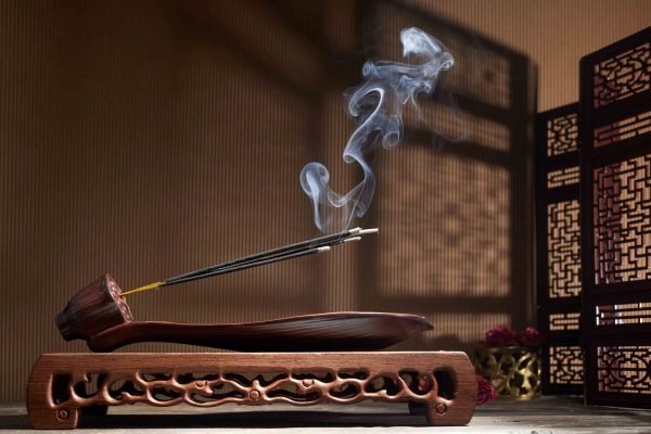 Smoke from burning incense sticks standing on lotus incense holder.